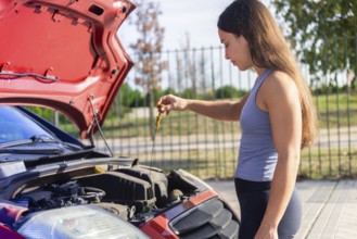 Young woman inspects a car engine on a sunny day The red car's hood is open, parked on a roadside