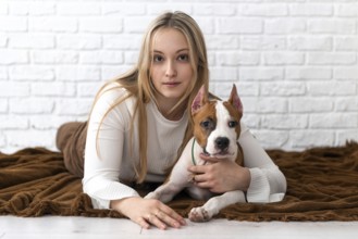A young woman with blonde hair lounges on a brown blanket, affectionately cuddling her white and