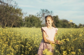 A young girl in a striped dress enjoys a peaceful moment in a blooming yellow flower field. She