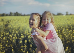 A young girl carries her little sister on her back as they laugh together in a field of bright