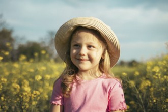 A young girl wearing a straw hat smiles warmly as she enjoys the golden sunlight in a beautiful