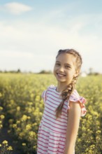 A young girl in a striped dress enjoys a moment of peace in a field of blooming yellow flowers.