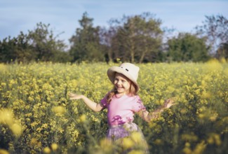 A little girl in a pink dress twirls happily among yellow flowers, embracing the beauty of nature