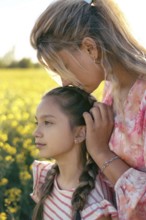 A mother gently kisses her daughter's forehead in a sunlit flower field, expressing love, care, and