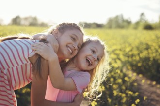 Two girls sisters play happily together in nature on a flowering field in summer