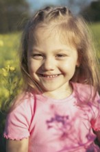 A young girl with bright eyes and a big smile enjoys a sunny day in a field of yellow flowers Her