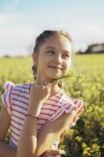 A young girl in a striped dress enjoys a peaceful moment in a blooming field, holding wildflowers