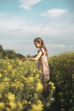 A young girl in a striped dress enjoys a peaceful moment in a blooming yellow flower field. She