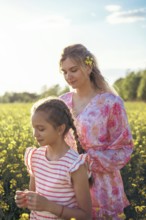 A mother and daughter spend quality time in a blooming yellow flower field, enjoying the warm