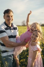 A young father and two daughters have fun together outdoors in the summer. Happy parenting and