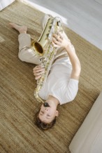 Young boy lying comfortably on a woven carpet and playing a saxophone. The cozy atmosphere