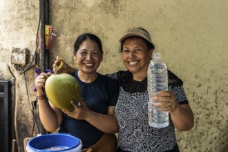 Two smiling asian women showcase a freshly opened coconut and a bottle of coconut water,