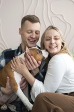 A cheerful young couple is seen enjoying a playful moment with their small brown and white dog in a