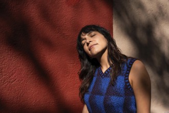 A Latin woman tilts her face toward the sunlight, eyes closed in a moment of relaxation. The warm