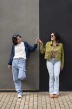 A joyful lesbian couple stands side by side, holding hands and smiling brightly while leaning