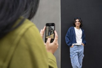 A lesbian couple enjoys a casual outdoor photoshoot. One woman wears denim and smiles against a