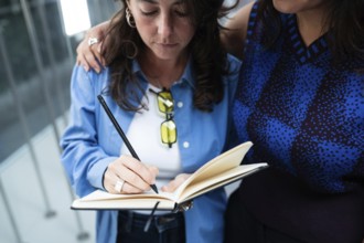 A lesbian couple shares a tender moment as one writes in a notebook while the other embraces her.