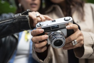 A lesbian couple shares a moment of connection through photography. Their hands hold a vintage