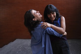 A joyful scene captures a multiethnic lesbian couple embracing and laughing together, celebrating