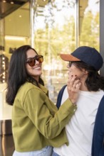 A lesbian couple shares a joyful moment in an urban setting. They wear casual outfits and