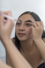 A woman concentrates while applying makeup using a brush in front of a mirror. The close up