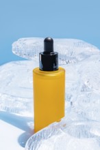 A vibrant yellow serum bottle with a black dropper, encased in clear ice blocks against a solid