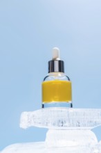 A cosmetic serum bottle with a dropper perched atop a block of ice, highlighted against a soft blue