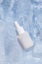 A frosted glass serum bottle with a dropper, cradled by sparkling chunks of ice, emphasizing