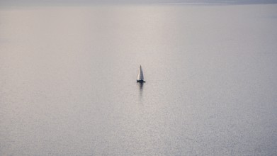 A solitary sailboat on the tranquil waters of Lake Geneva during a sunny winter day, with the snowy