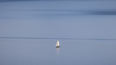 A lone sailboat glides over Lake Geneva on a clear winter's day, framed by the vineyards of Lavaux