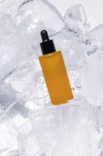 A vibrant, yellow serum bottle with a dropper, artfully encased in glistening ice cubes,