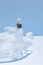 A frosted glass serum bottle with a dropper, resting in a carved ice block on a vibrant blue