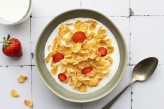 A bowl of crunchy cornflakes with fresh strawberry slices, served in milk. A wholesome breakfast