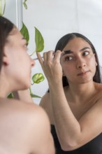 A woman focuses on applying makeup with a brush in front of a mirror for the makeup session. A