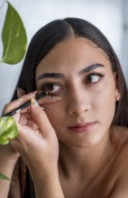 A woman applies eyeliner with precision, focusing intently. Her delicate hand grips the pencil,
