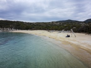 A peaceful aerial view of Kalamitsi wild beach in Greece. A couple sits on the golden sand by