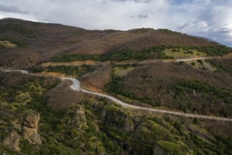 A road cuts through the autumn landscape of Meteora. Surrounded by lush hills and towering rock