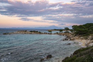Karydi Beach in southern Greece at sunset, featuring turquoise waters, rocky shores, and scattered