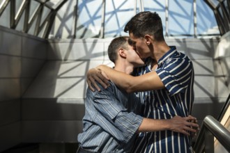 Romantic gay couple embracing and sharing a kiss in a modern architectural setting. Soft light and