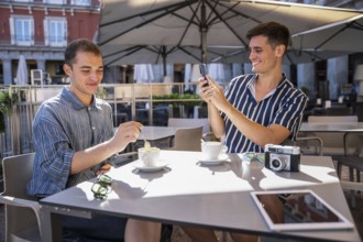 Gay couple enjoying coffee at an outdoor cafe in Plaza Mayor, Madrid. One stirs his coffee while