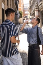 Gay couple pausing for a water break on a sunny street in Madrid. One drinks from a bottle while