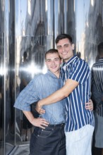 A smiling gay couple embraces in the lively streets of Madrid, reflecting the vibrant and inclusive
