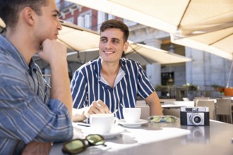 A loving gay couple enjoys a sunny coffee date on the vibrant streets of Madrid, capturing moments
