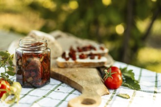 A rustic scene of canapes being prepared. Fresh tomatoes, a jar of preserved vegetables, and bread