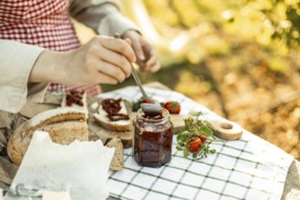 A person spreads sun-dried tomatoes on bread slices for canapes. The setup is outdoors with fresh