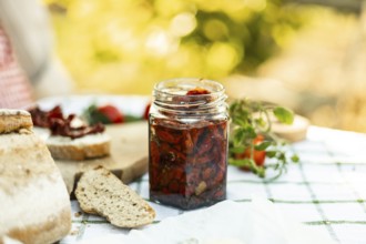 A rustic outdoor setting featuring a jar of homemade sun-dried tomatoes, fresh bread, and ripe