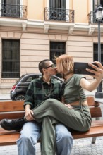 Colombian lesbian couple captures a loving kiss on a city bench, showcasing affection and identity.