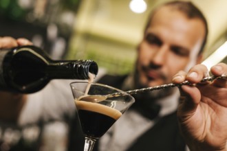 A skilled bartender expertly pours a drink into a glass, showcasing precision and flair. The