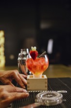 A professional bartender skillfully prepares a vibrant cocktail garnished with a fresh strawberry
