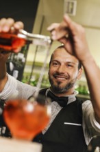 A professional bartender skillfully pours a vibrant cocktail in a busy bar. The image captures the